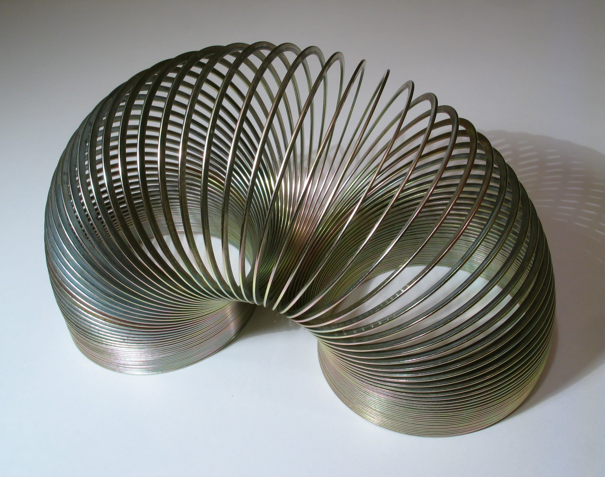 A metal coil toy arched on a white surface.
