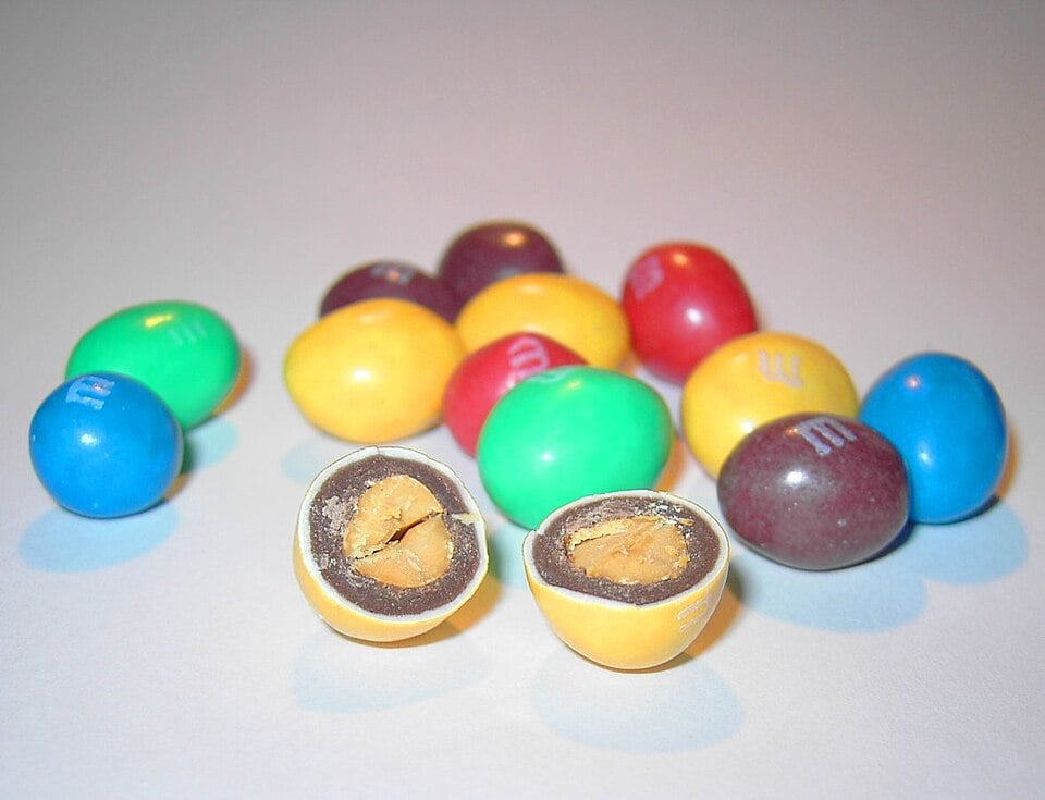 A pile of multicolored M&M’s, with two halves of a yellow peanut M&M in the foreground showing its chocolate and peanut center.
