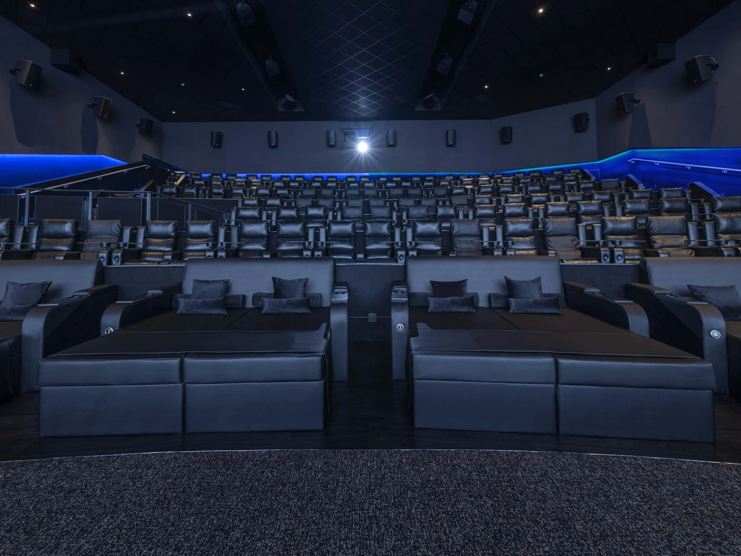 Empty movie theater with rows of black leather seats and large reclining loungers in the front.