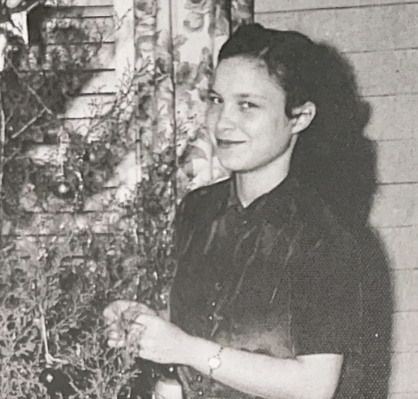 A young woman smiling while standing beside a Christmas tree.