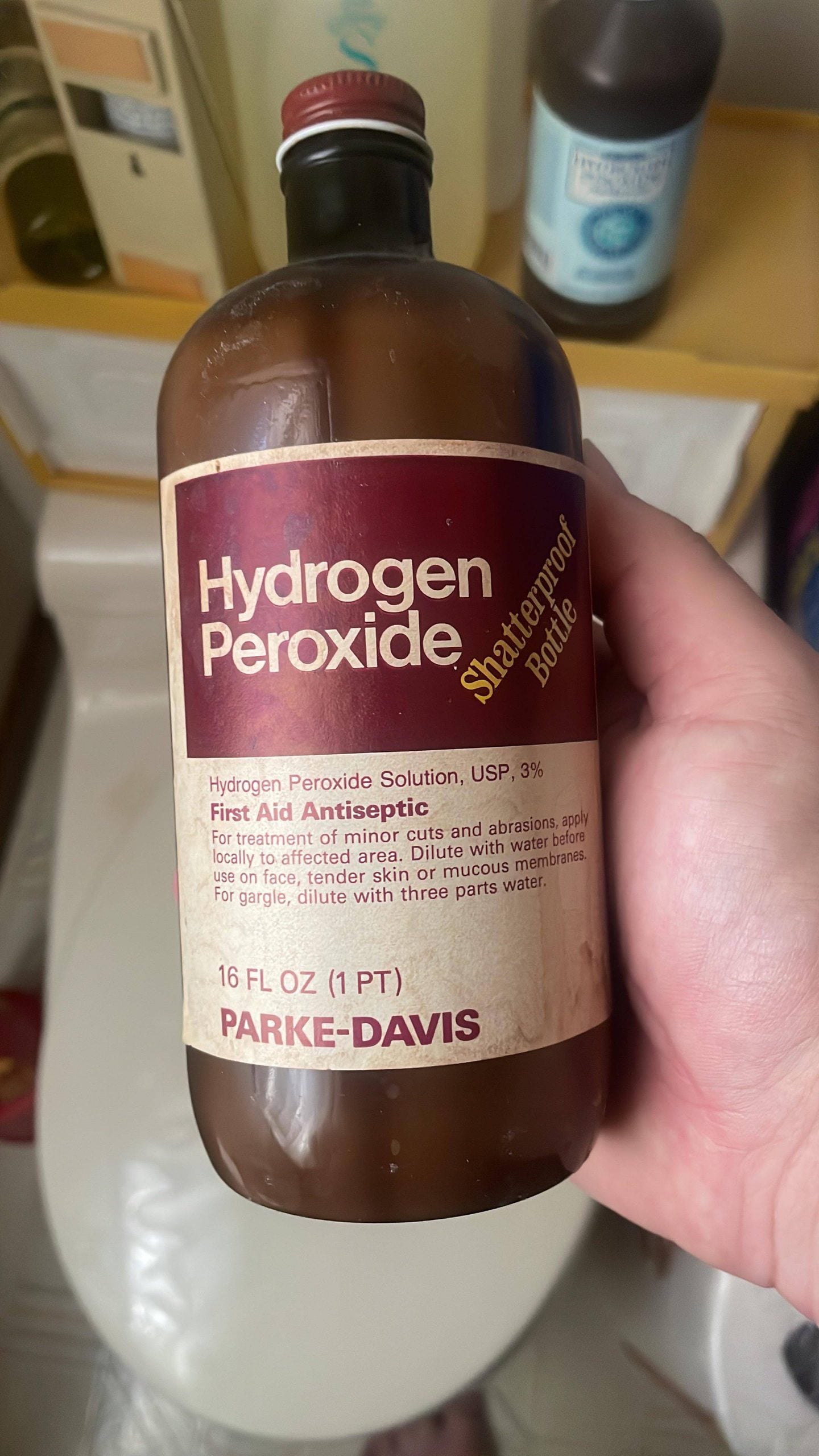 A hand holding a brown glass bottle of Parke-Davis Hydrogen Peroxide antiseptic solution.