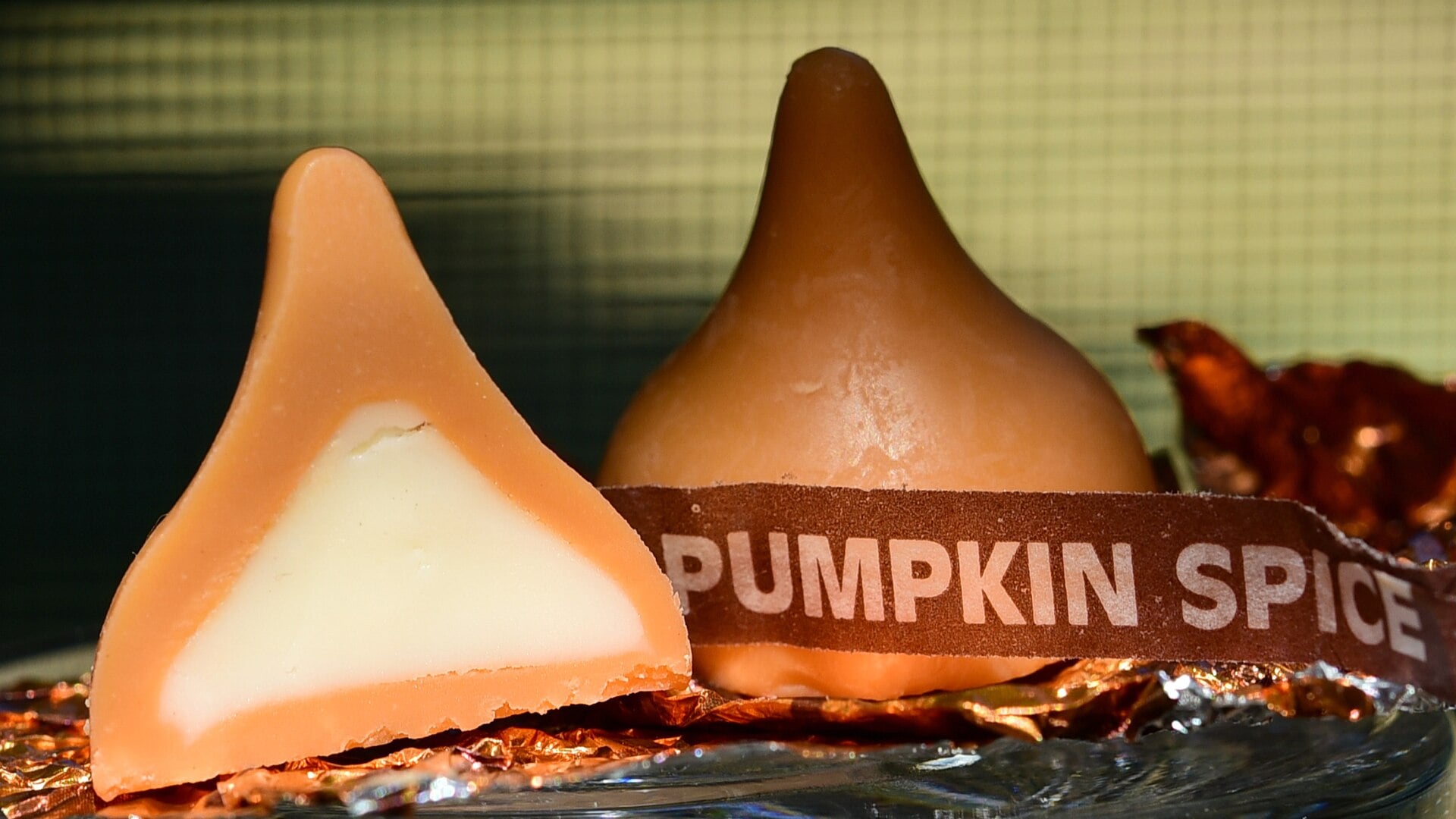 Two Pumpkin Spice Hershey’s Kisses, one halved to reveal a white center and one wrapped with a tag reading “PUMPKIN SPICE.”
