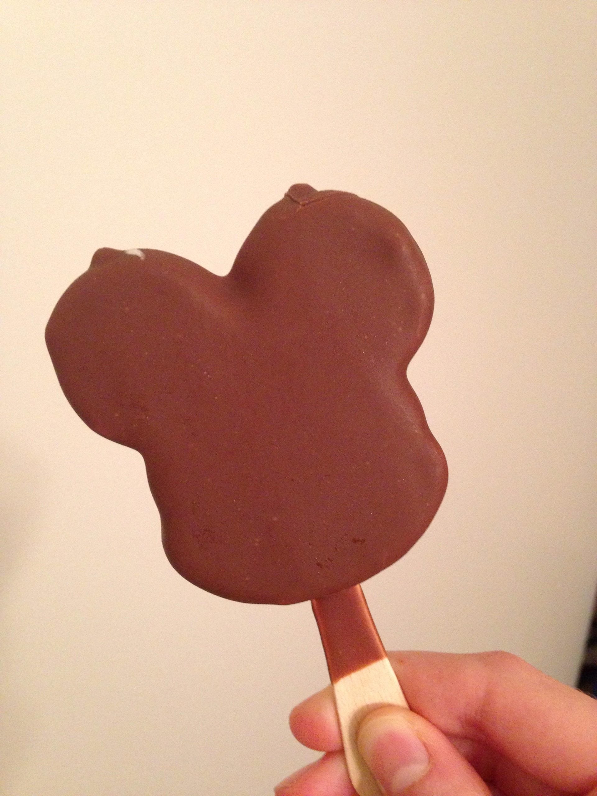 A hand holding a chocolate-covered ice cream bar shaped like Mickey Mouse.