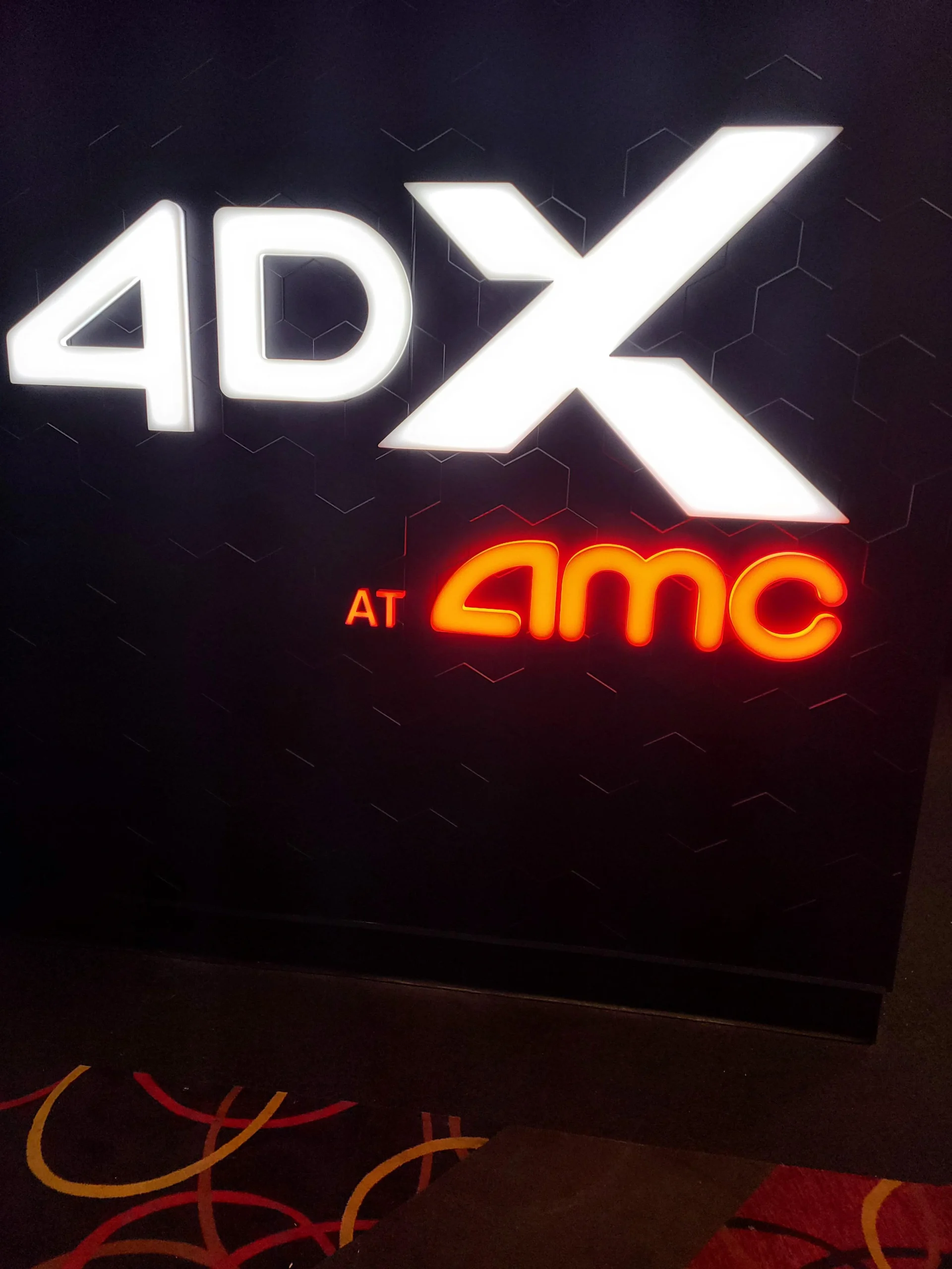 Illuminated 4DX sign above a glowing red AMC logo on a dark, patterned wall.