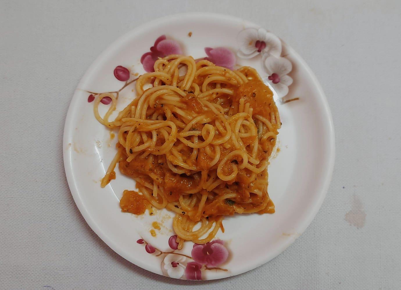 A serving of spaghetti with tomato sauce is placed on a white plate decorated with pink and purple flowers, set on a light-colored tablecloth.