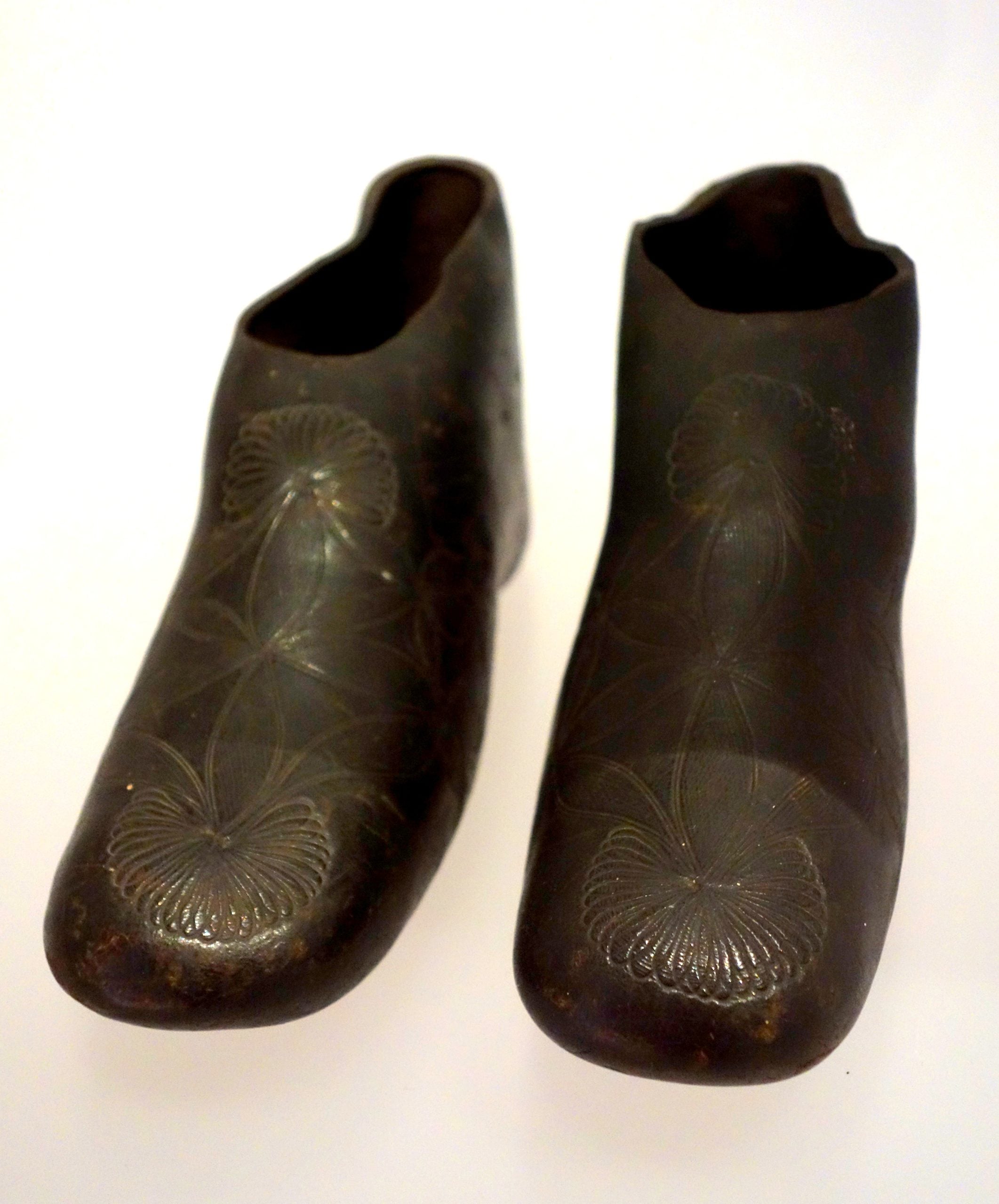 A pair of dark, carved wooden shoes with floral-like patterns on the toes and vamps.
