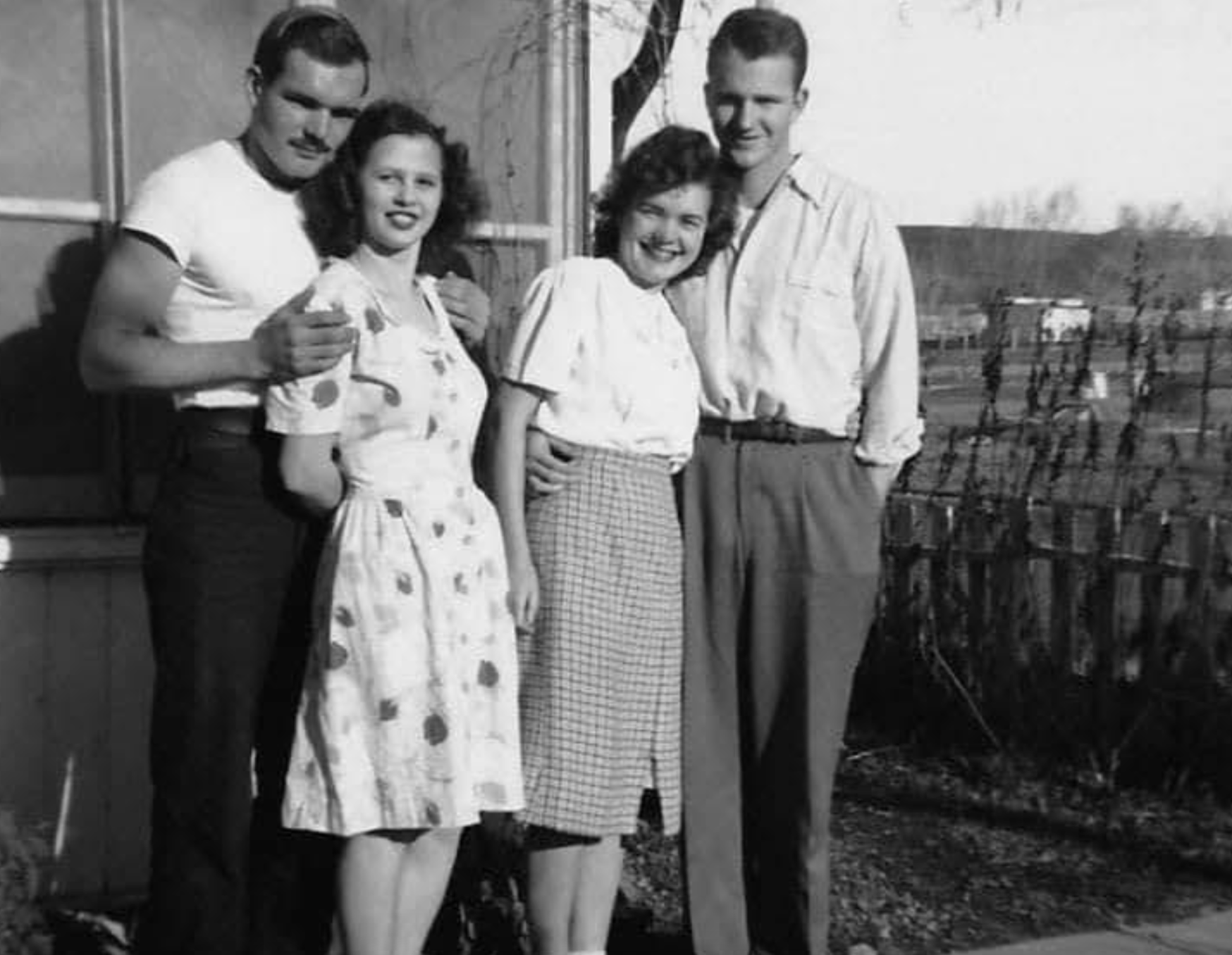 Two couples standing side by side outdoors in a black and white photograph.