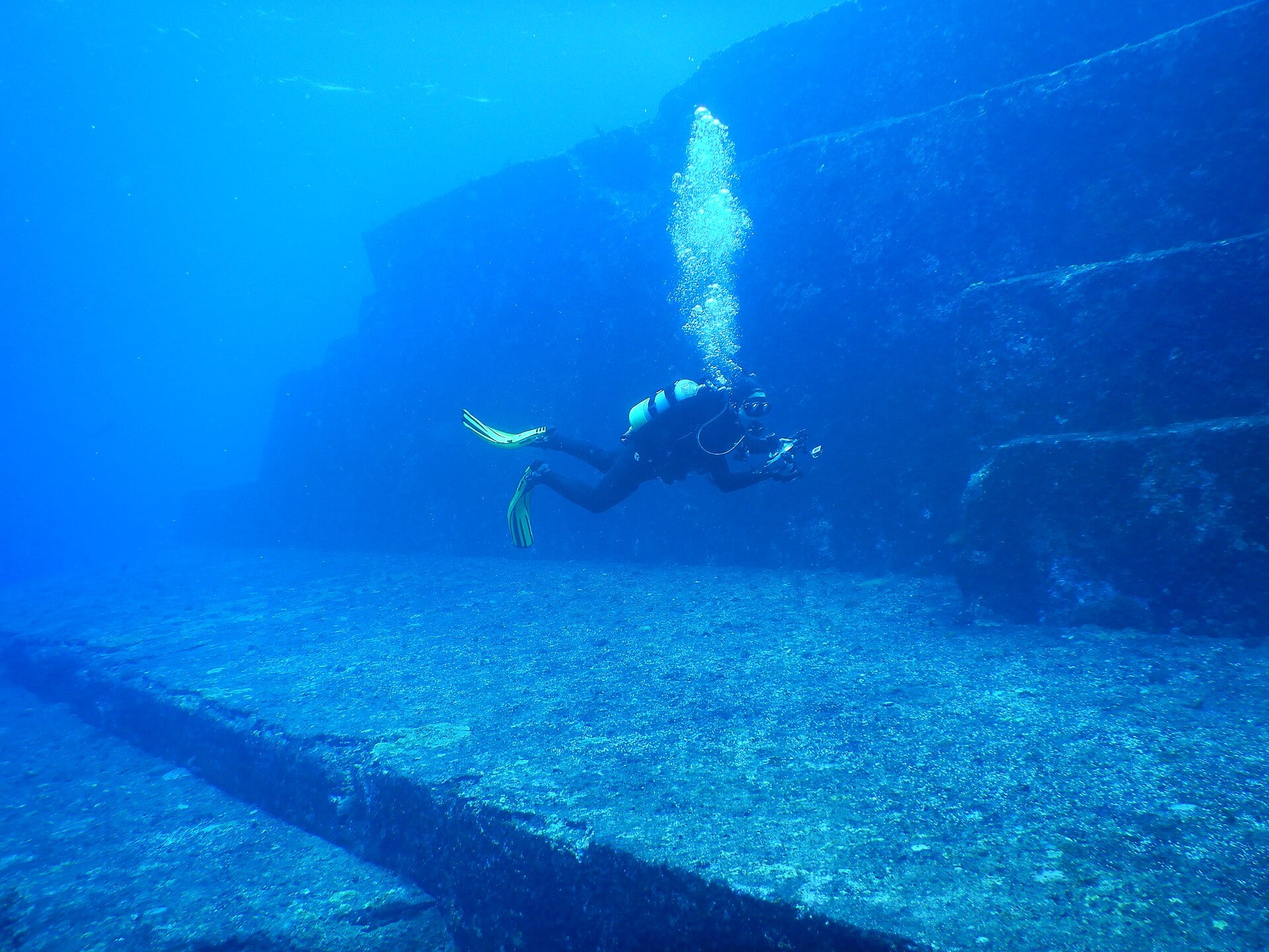 A scuba diver swims past a large, tiered underwater stone structure.