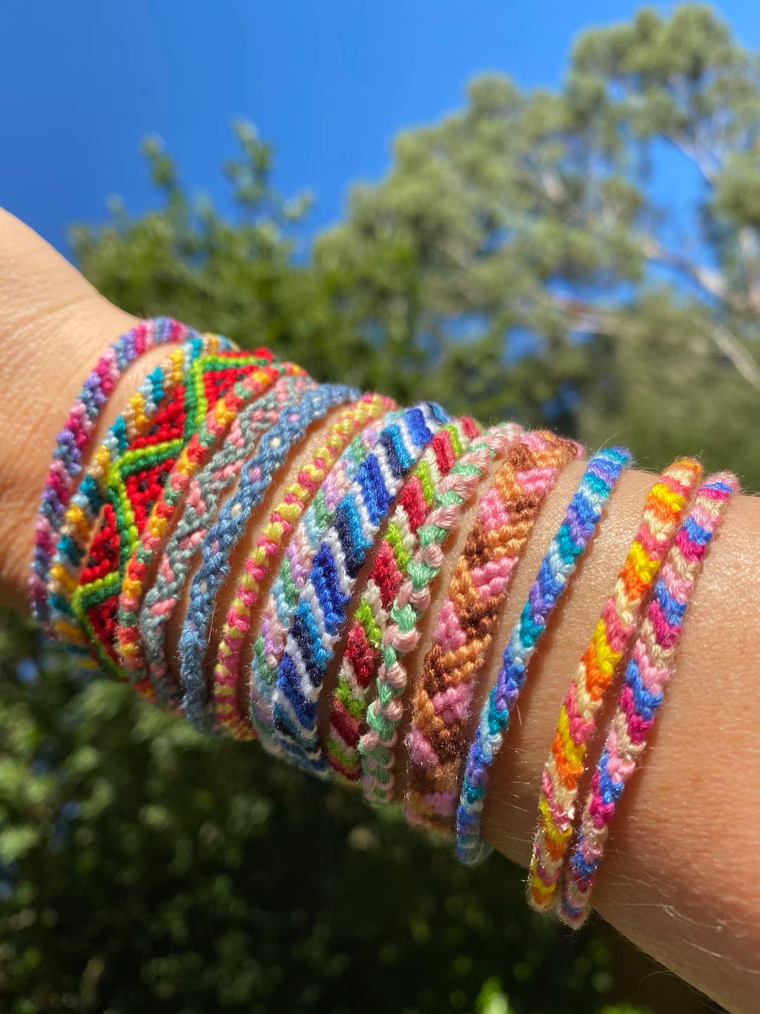 A forearm wearing a stack of colorful, hand-knotted friendship bracelets in various geometric patterns.
