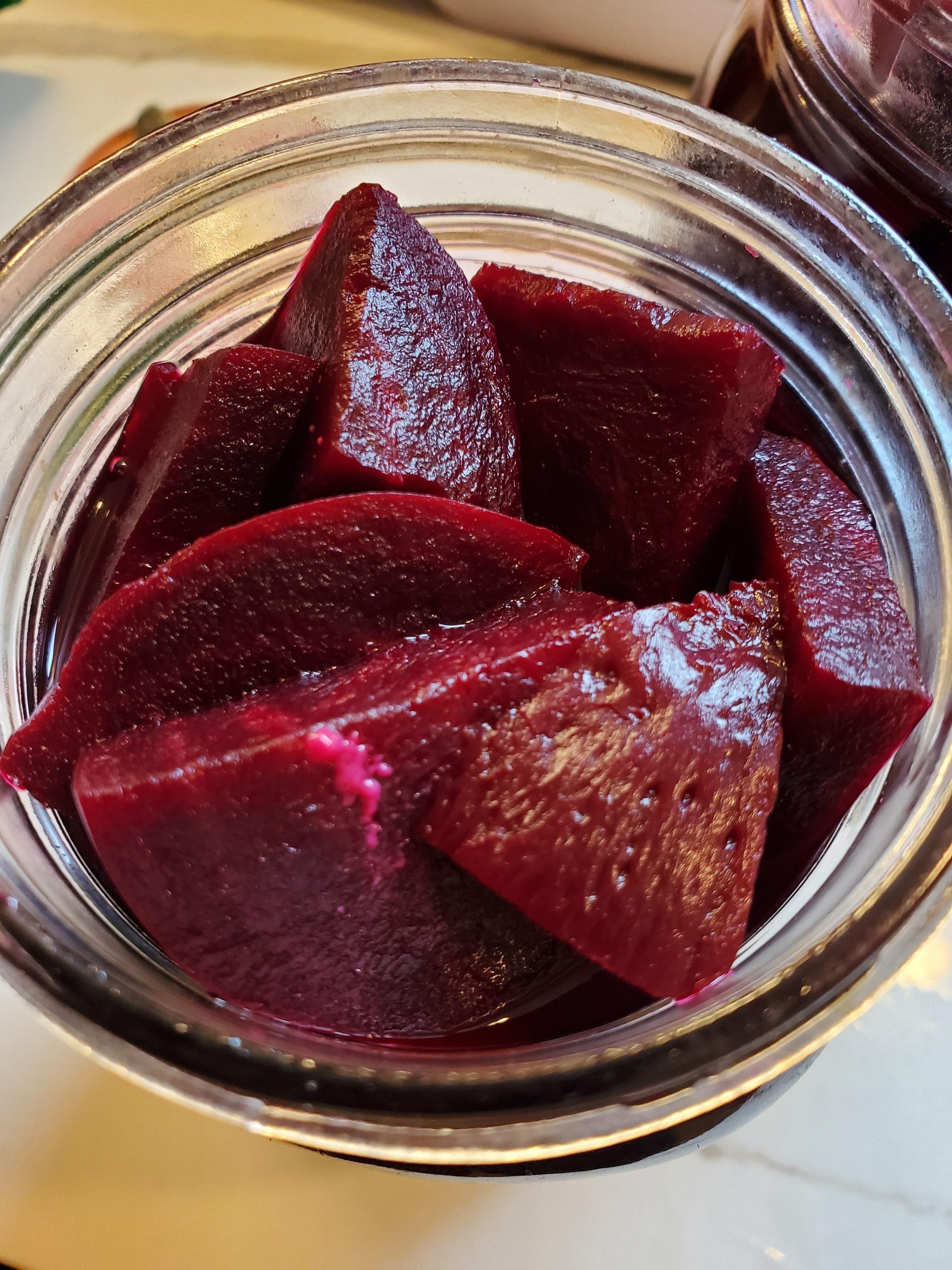 A glass jar filled with thick, sliced pieces of deep red pickled beets, sitting on a light-colored surface.