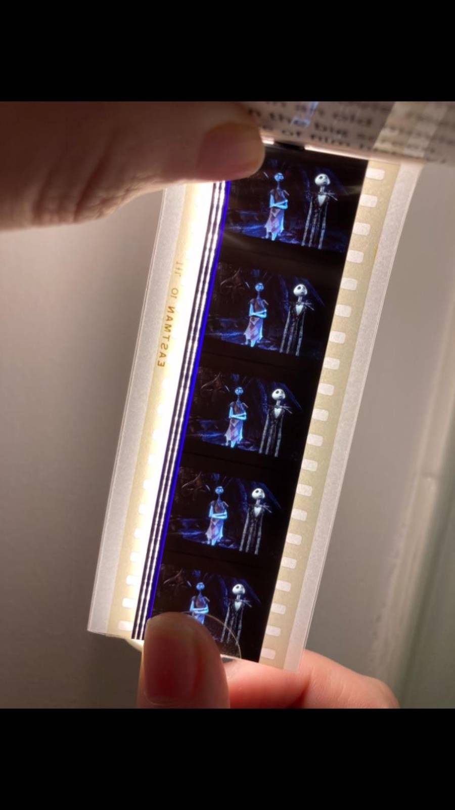 A hand holds up a strip of 35mm film frames featuring characters Jack Skellington and Sally from The Nightmare Before Christmas against a light source.
