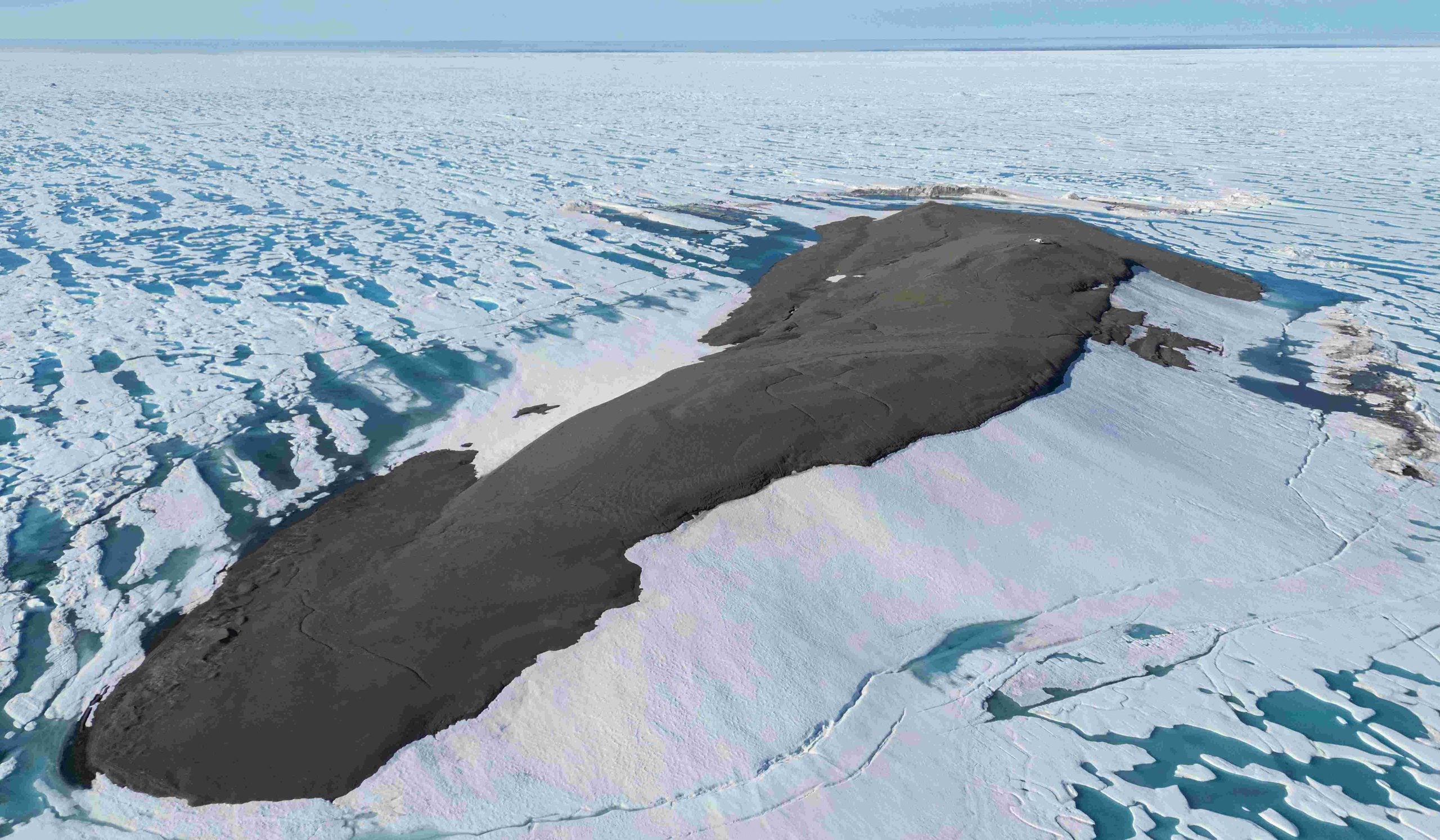 An aerial view of a dark, rocky island surrounded by a vast expanse of cracked sea ice.