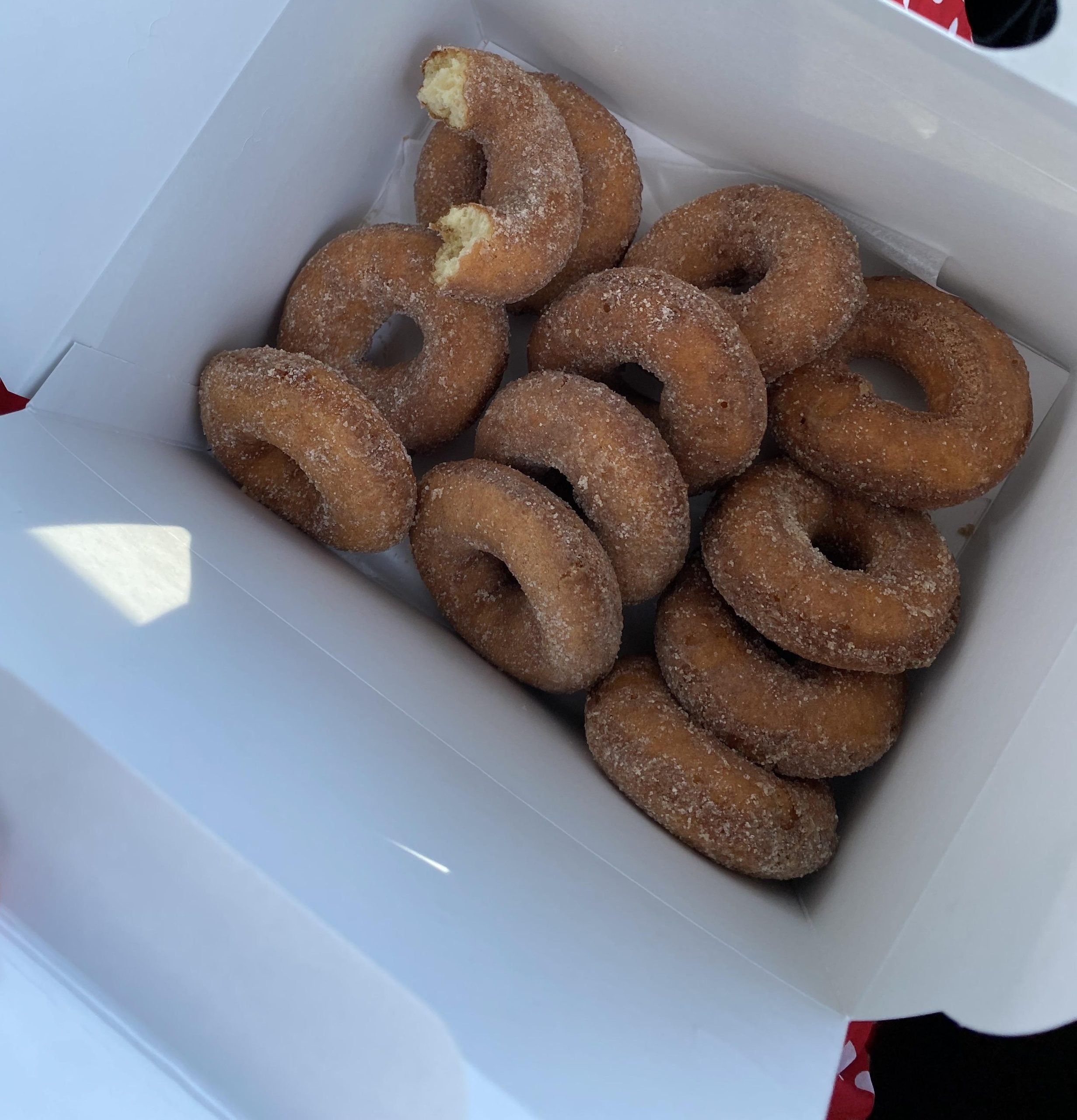 A box of cinnamon sugar-coated cake donuts, one with a bite taken out of it.