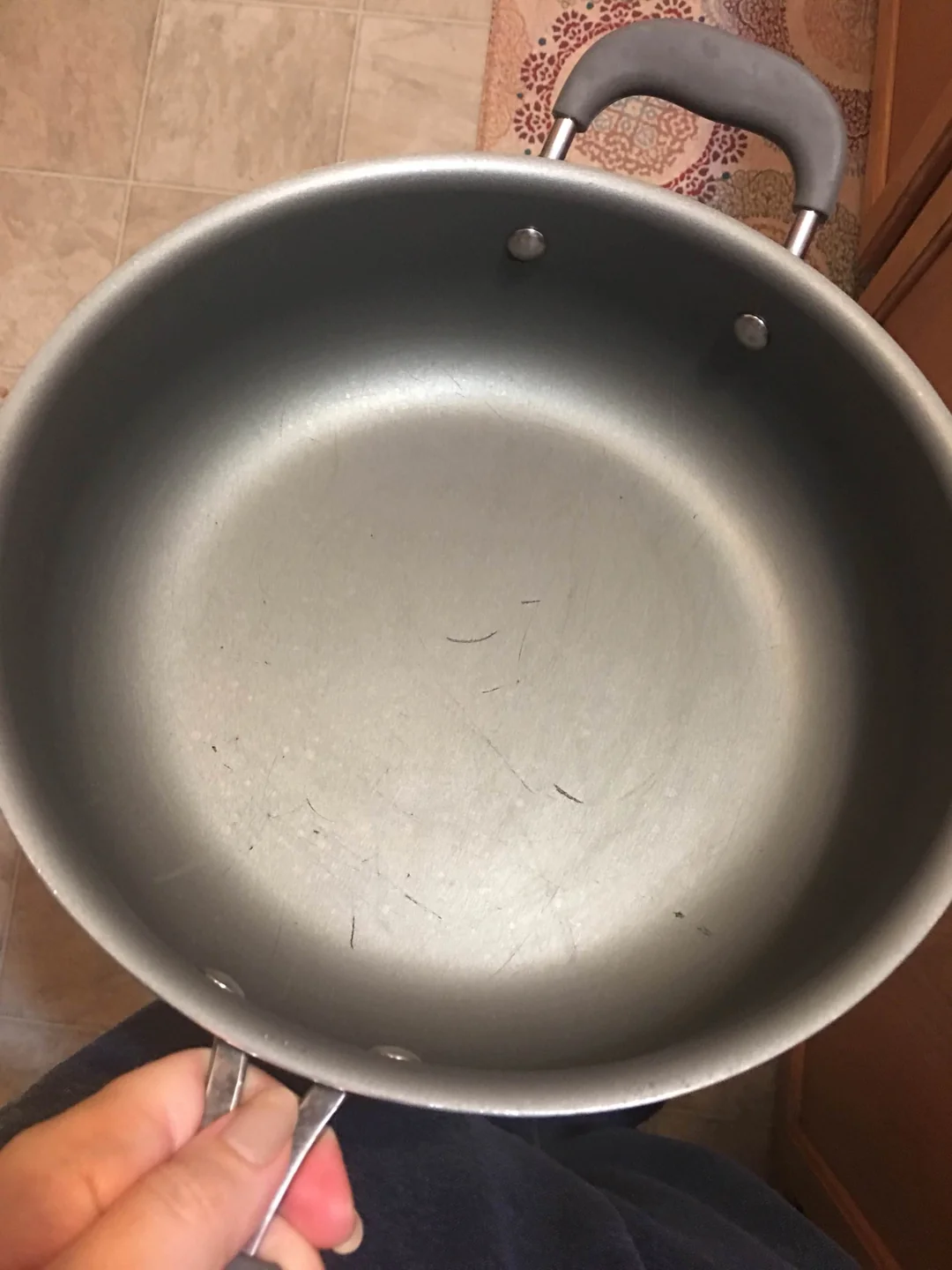 A hand holding a round, gray non-stick skillet with light surface scratches.