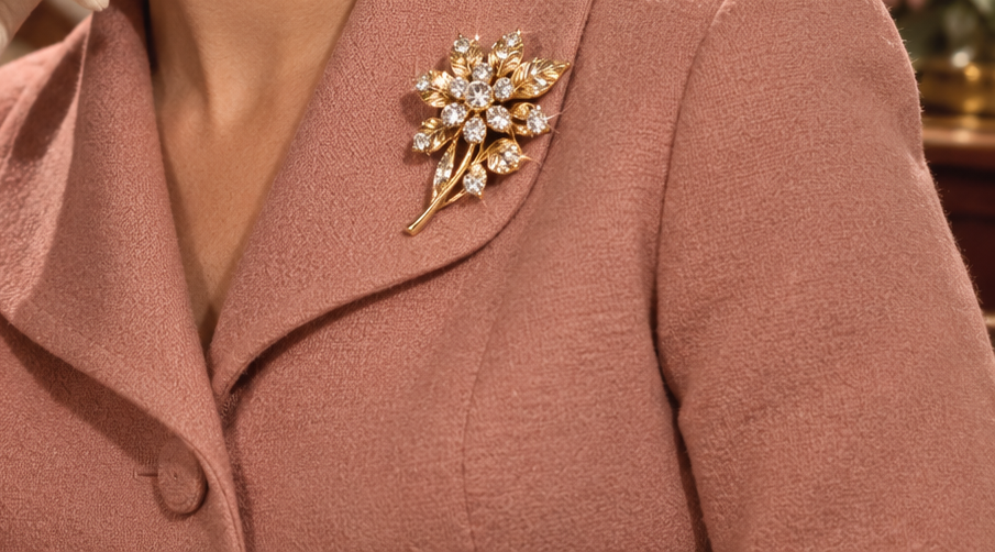 A gold flower brooch with rhinestone petals pinned to the lapel of a pink jacket.