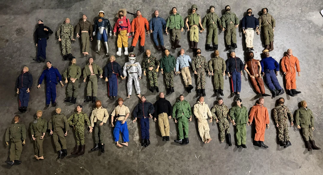 Forty-six vintage action figures in assorted military and uniform outfits are arranged in rows on a concrete floor, some with missing hands or feet, in various poses.