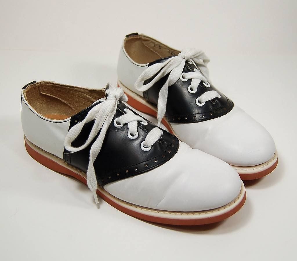 Pair of white and black saddle shoes with white laces and red soles.