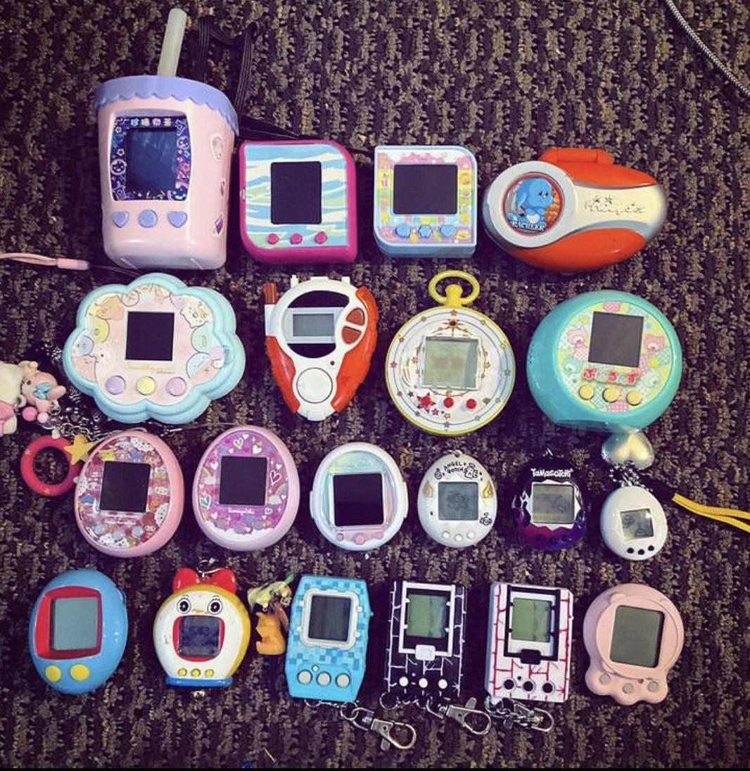 A large collection of colorful, various-shaped virtual pet keychain games arranged on a carpeted surface.