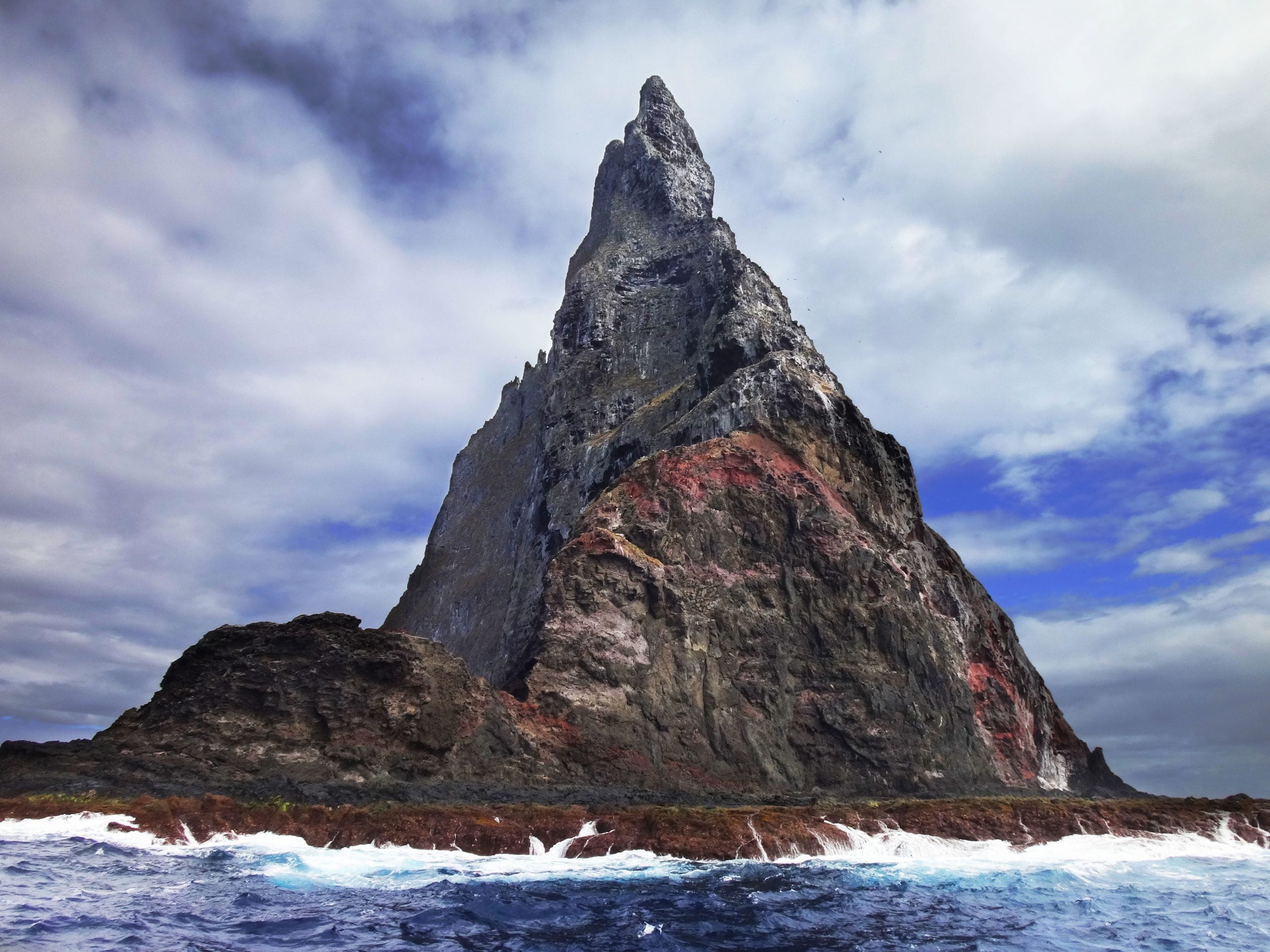 A towering, pointed volcanic rock formation rises steeply from the ocean.