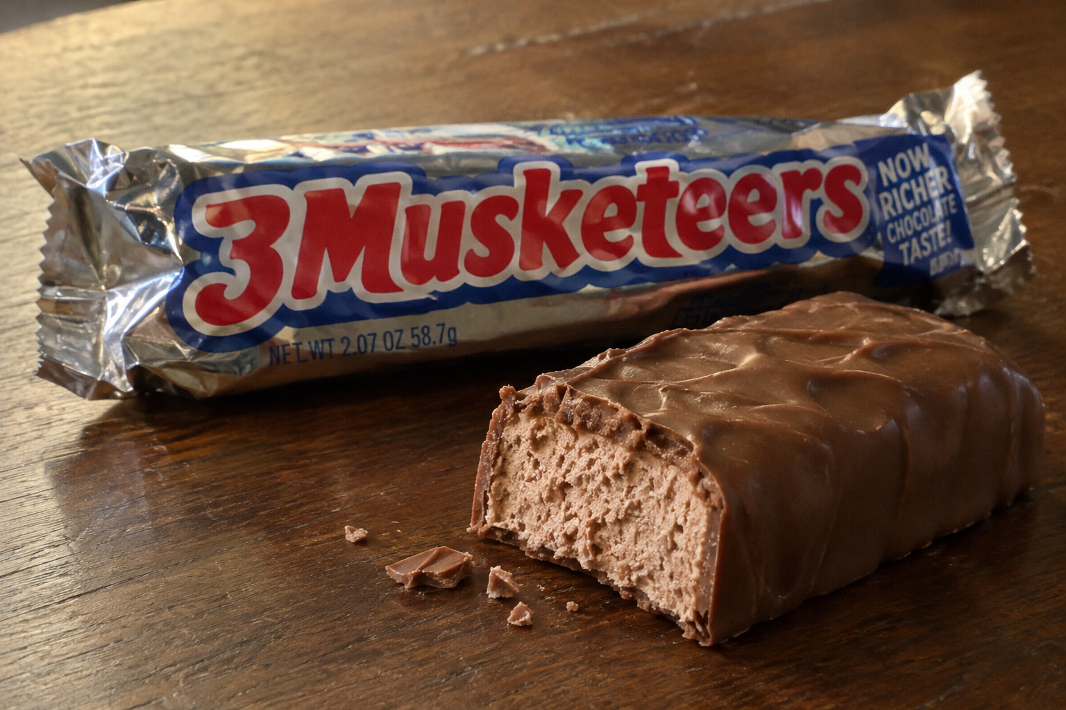 A 3 Musketeers candy bar with a bite taken out of it, resting in front of its silver wrapper.