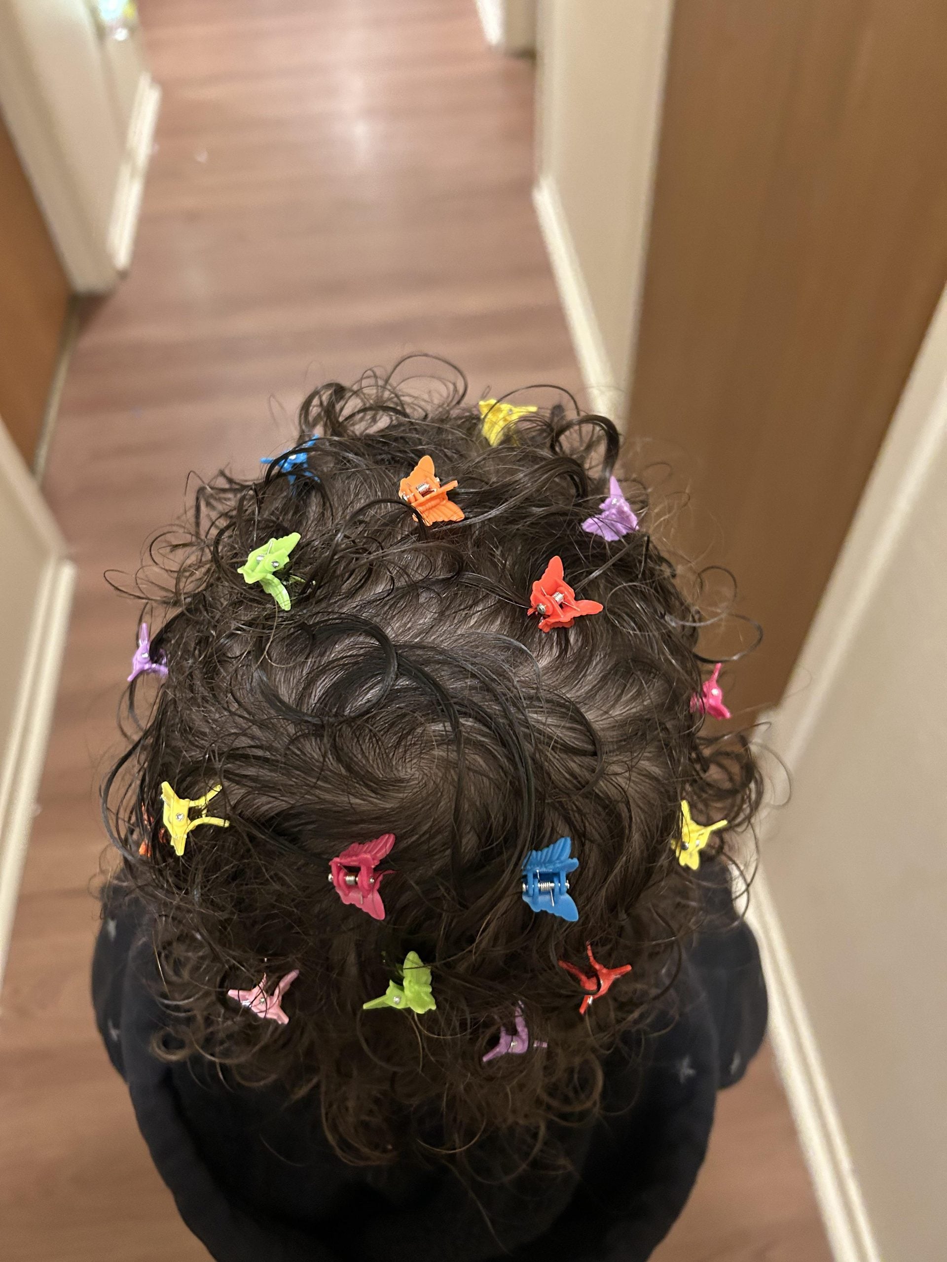 A child with curly dark hair decorated with many colorful butterfly-shaped hair clips.
