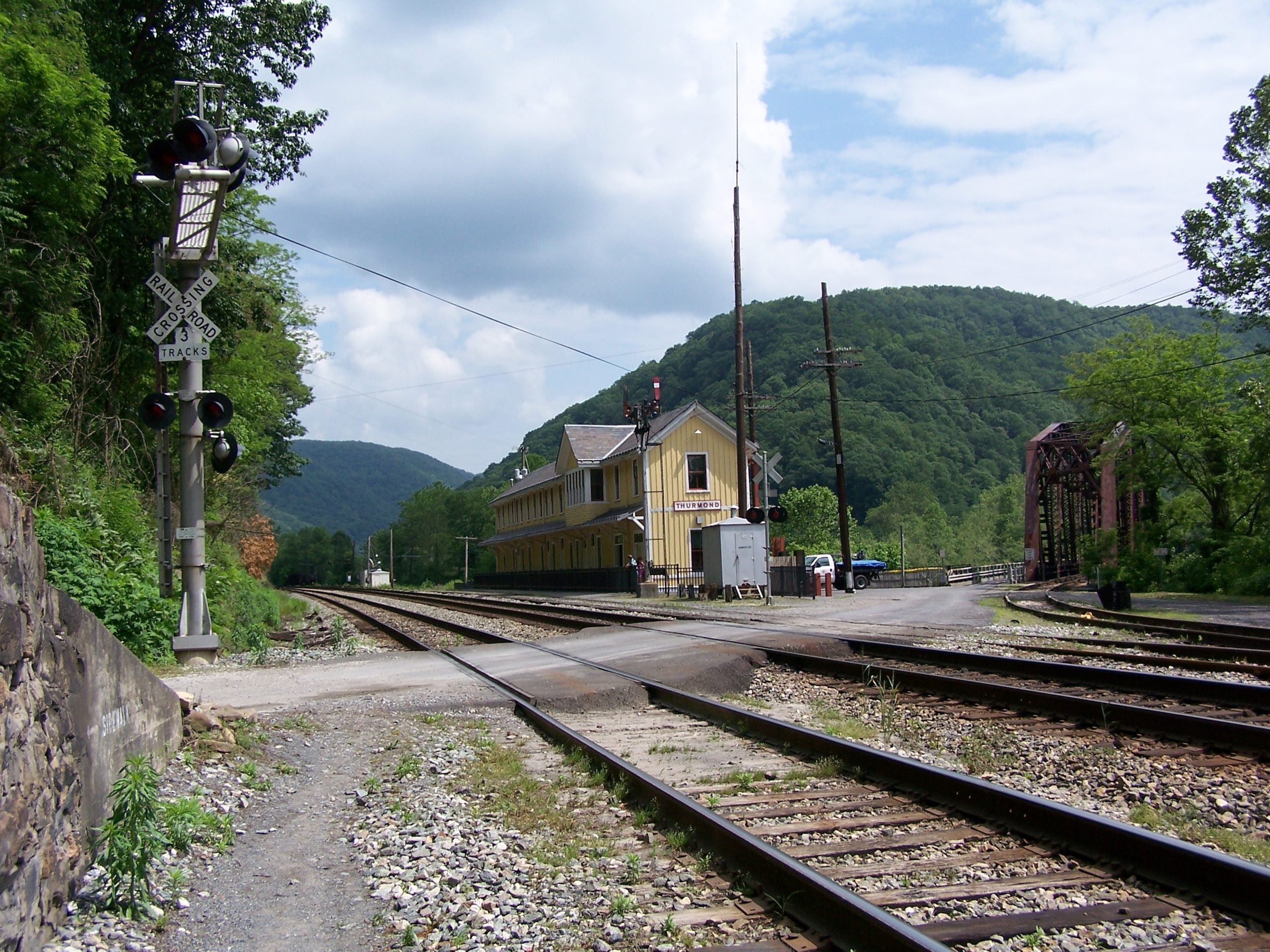A yellow train depot labeled “Thurmond” beside multiple railroad tracks and a bridge in a mountain valley.