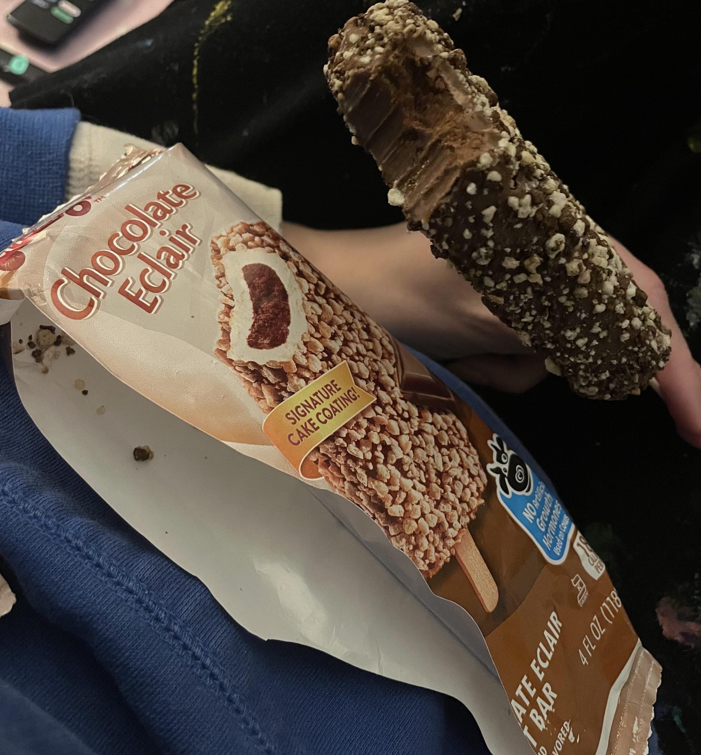 A half-eaten chocolate eclair ice cream bar next to its open wrapper.