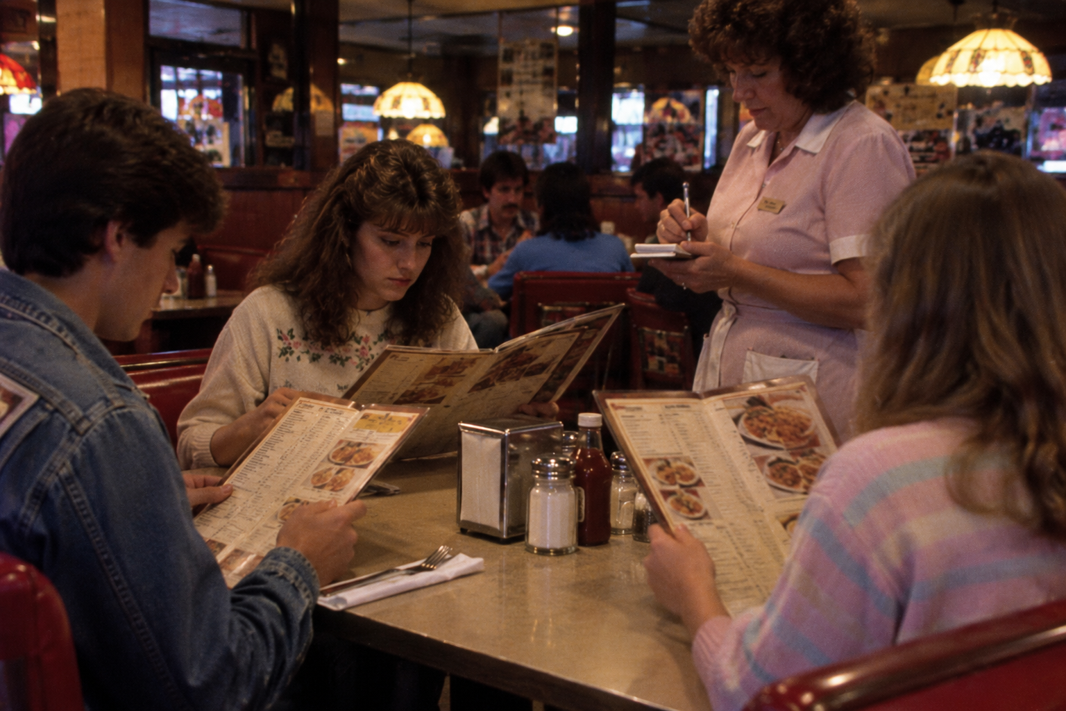 A waitress takes an order at a table in a diner as three customers look at their menus.