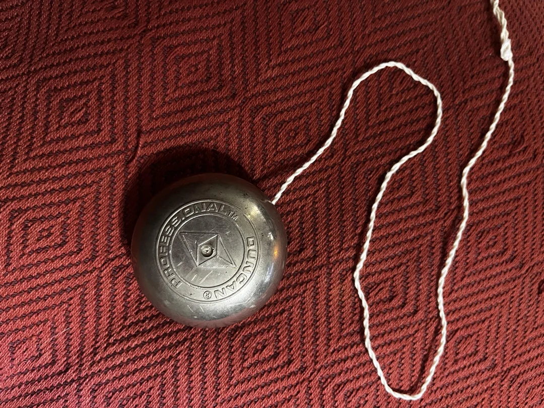 A silver Duncan Professional yo-yo with its white string extended, resting on a textured red surface.