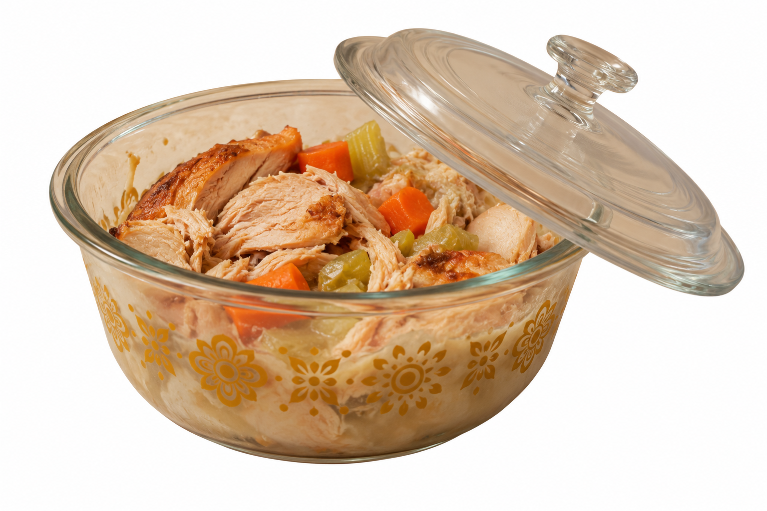 A glass casserole dish containing shredded cooked chicken, carrots, and celery, with the glass lid resting partially off the top.