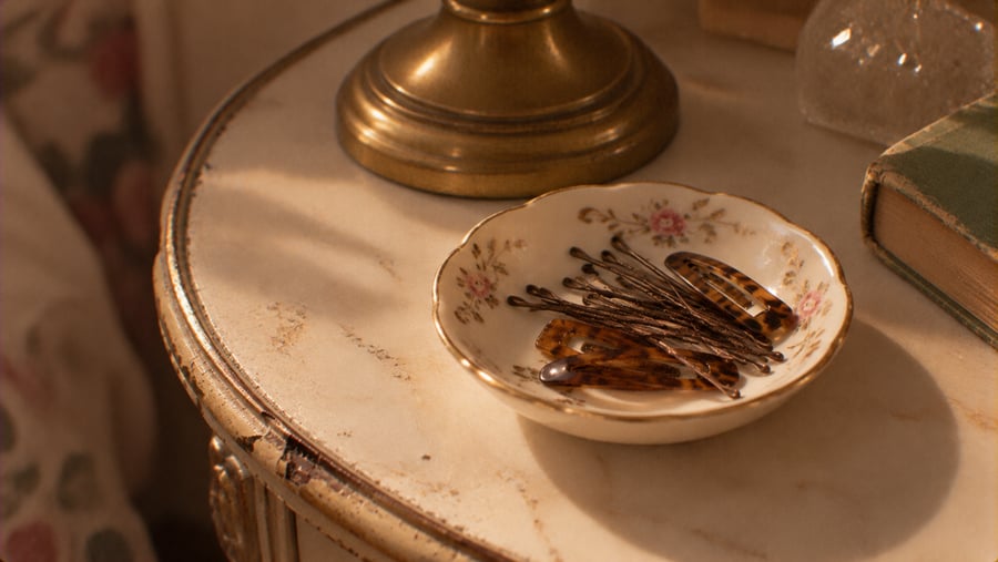 A small, floral-patterned ceramic dish on a nightstand containing bobby pins and hair clips.