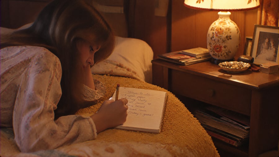 A young person lying on a bed writing a to-do list in a spiral notebook.