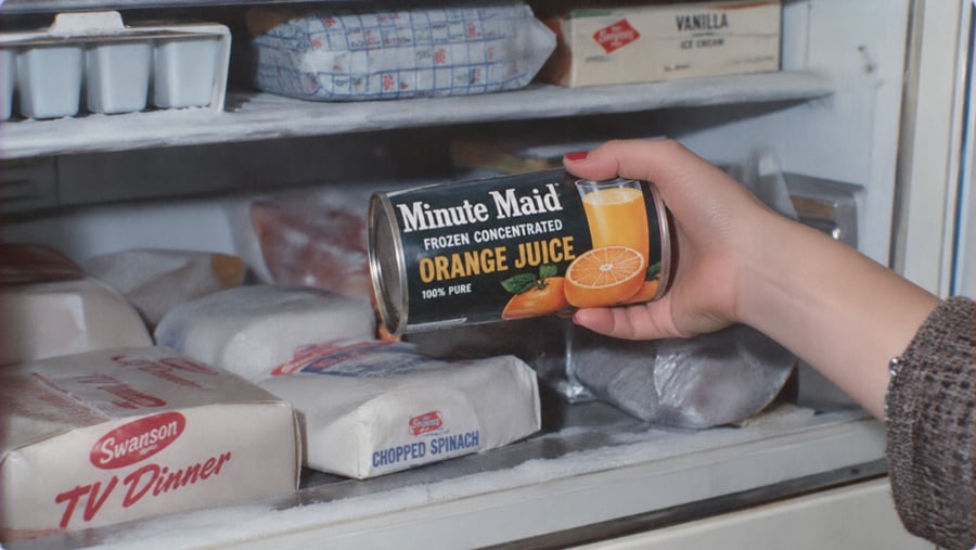 A hand reaches into a freezer to select a can of Minute Maid frozen concentrated orange juice.
