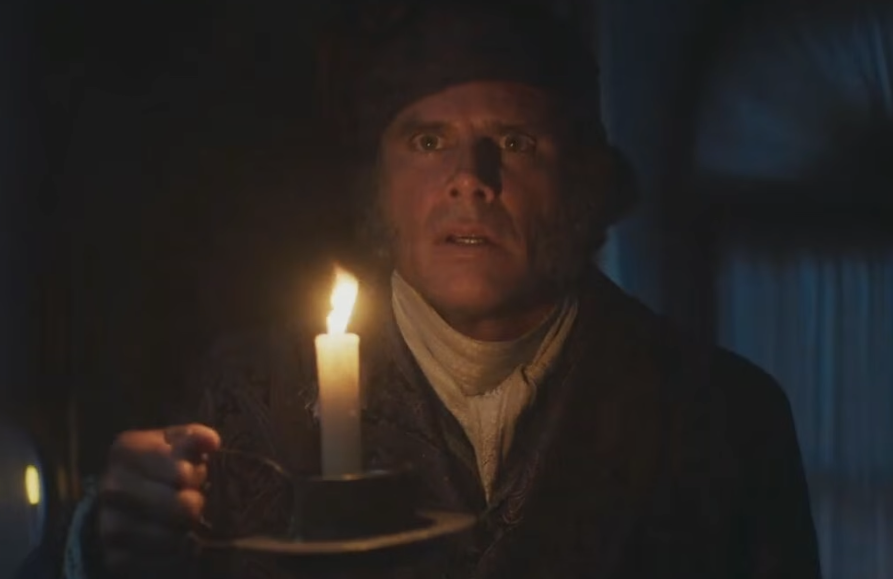 A man in period clothing holds a lit candle and looks ahead with a surprised expression.