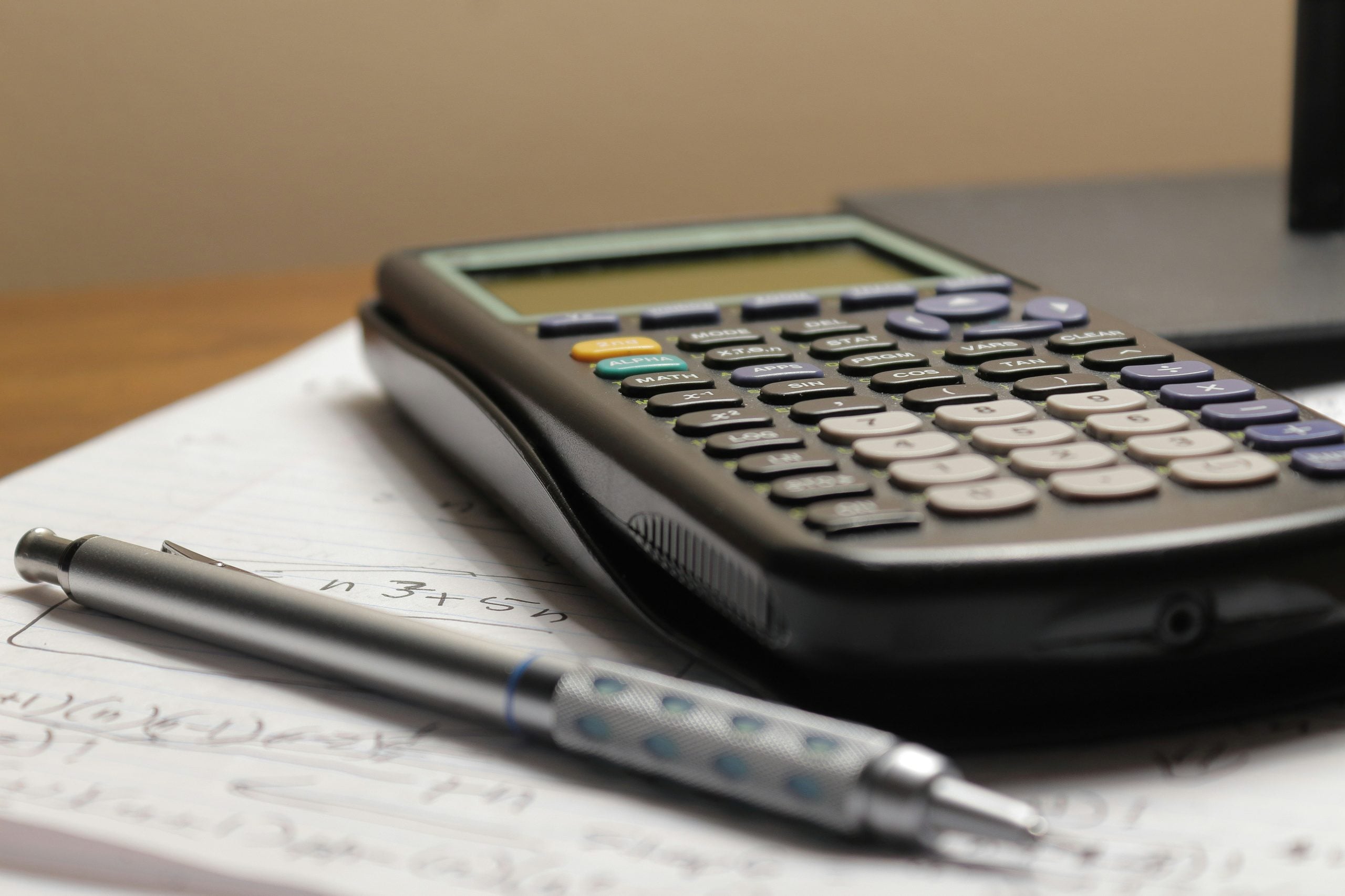 A graphing calculator and a mechanical pencil resting on a sheet of handwritten math problems.