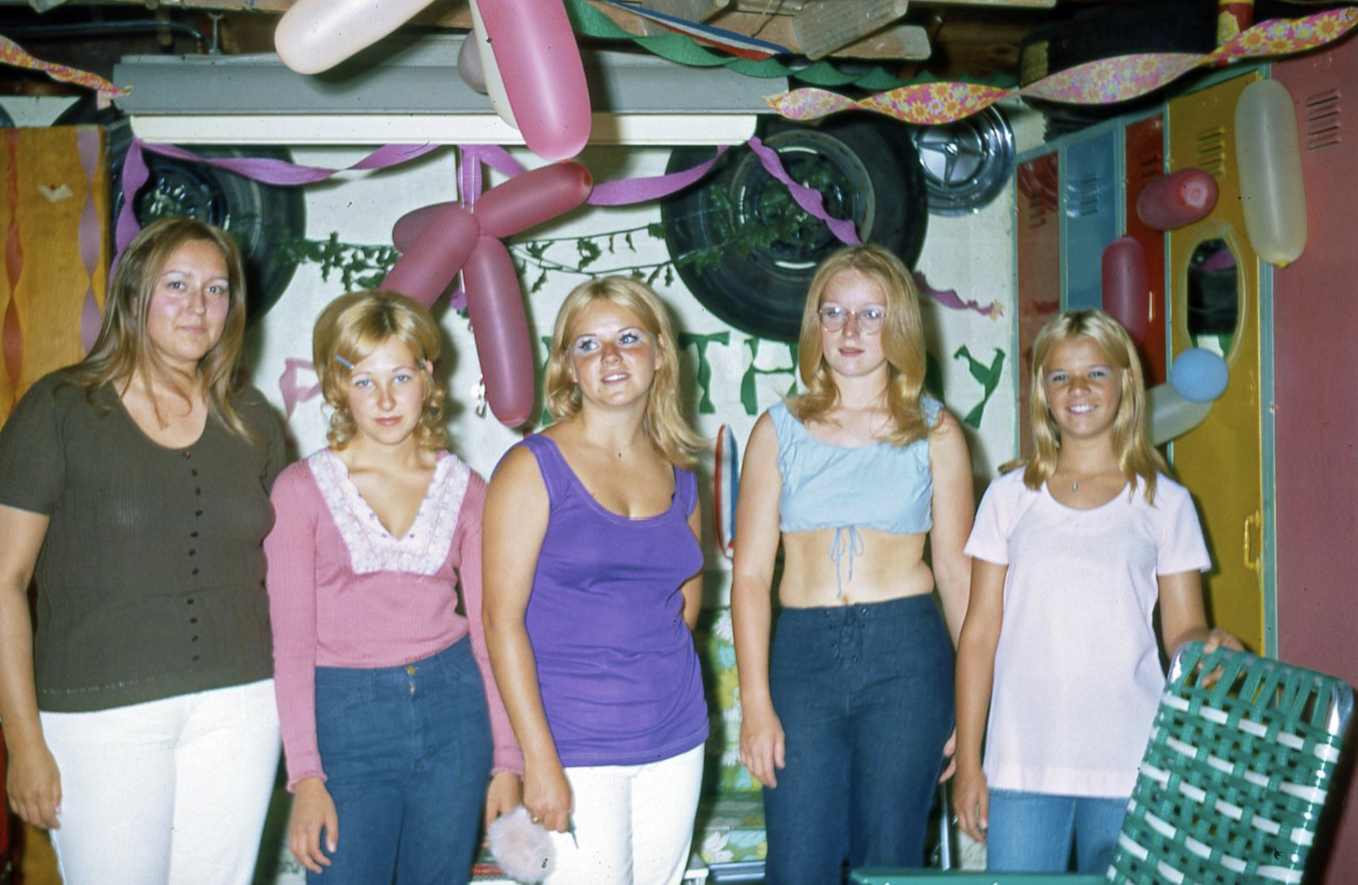 Five young women posing for a photograph in a room decorated with balloons and streamers.