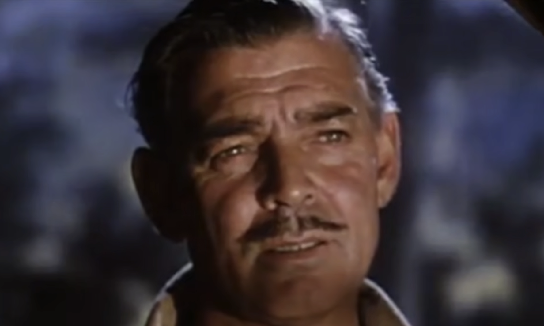 A close-up portrait of Clark Gable with a thin mustache, looking off-camera.