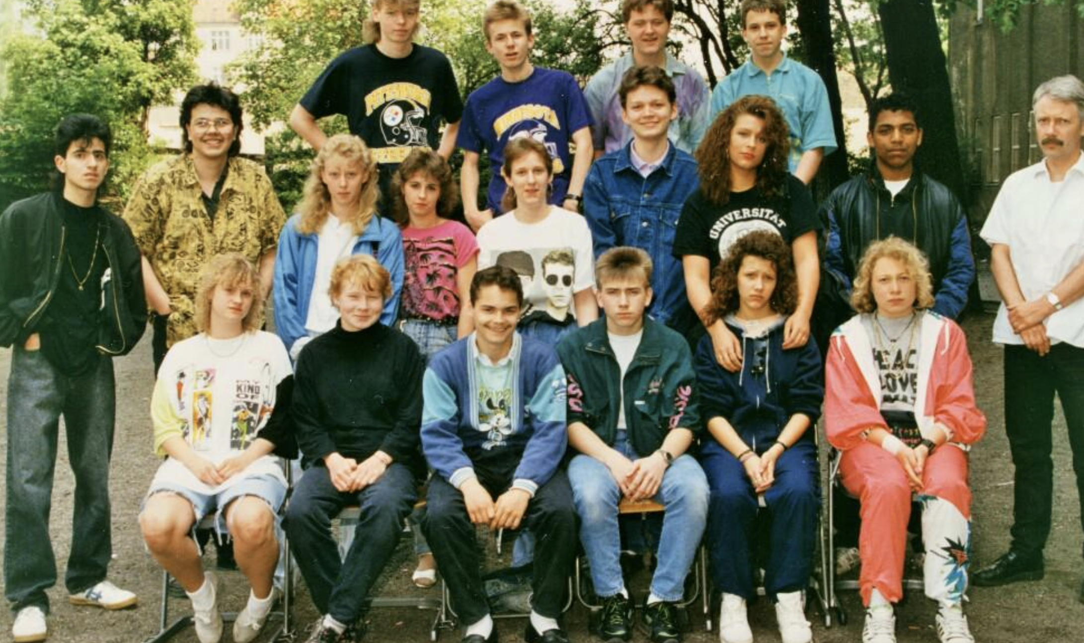 A high school class photo of sixteen students and their teacher posing outdoors.