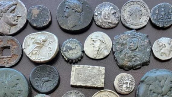 A collection of various ancient coins, including circular and rectangular pieces with embossed portraits, animals, and inscriptions.