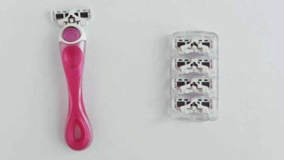 A pink razor handle with a blade attached, next to a clear plastic cartridge case containing four replacement razor blade heads.