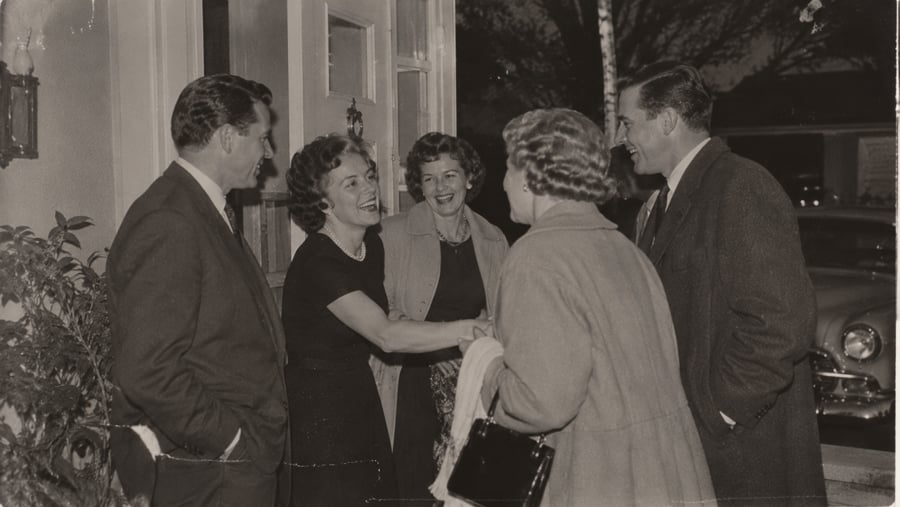 Two couples greeting each other outside a home at night.