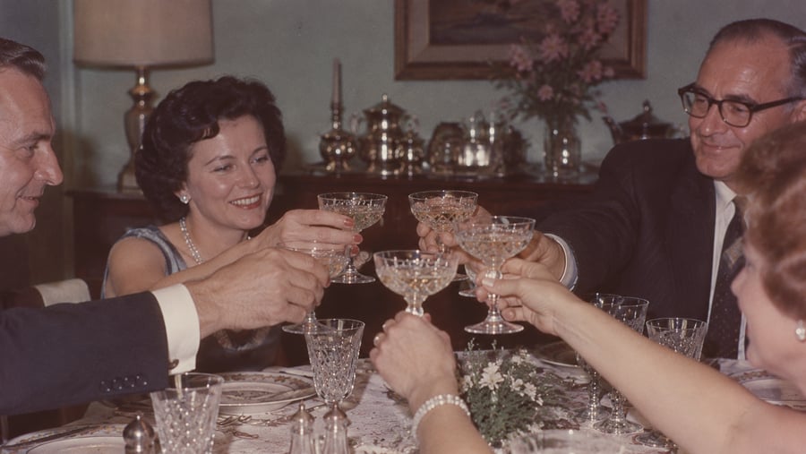 Four people around a dining table raise their crystal glasses in a toast.
