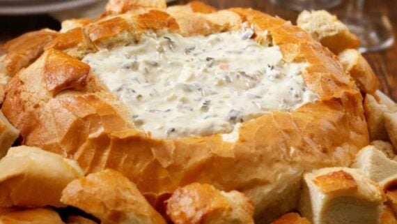 Creamy dip served inside a hollowed-out loaf of bread, surrounded by bread chunks for dipping.