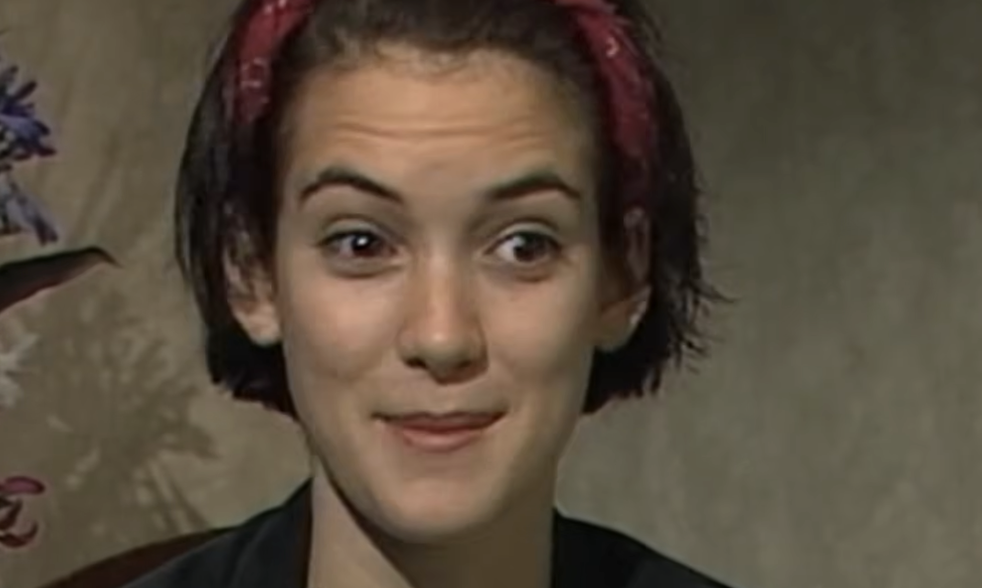 A young woman with short dark hair and a red headband looking forward with a wide-eyed, surprised expression.