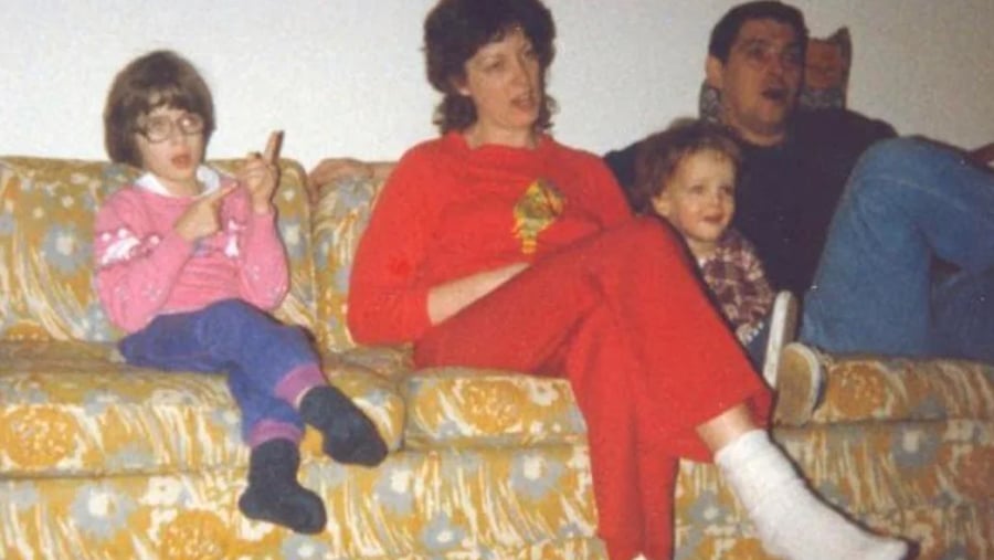 A family of four sits on a floral patterned couch.