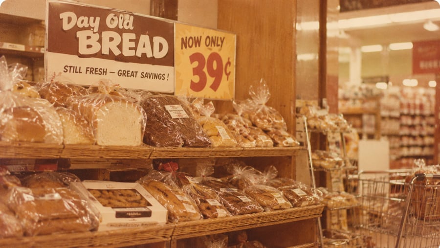 Shelves of packaged bread in a grocery store under a sign advertising “Day Old Bread” for 39 cents.