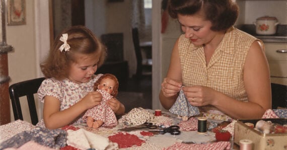 A woman and a young girl sitting at a table sewing small outfits for a doll.