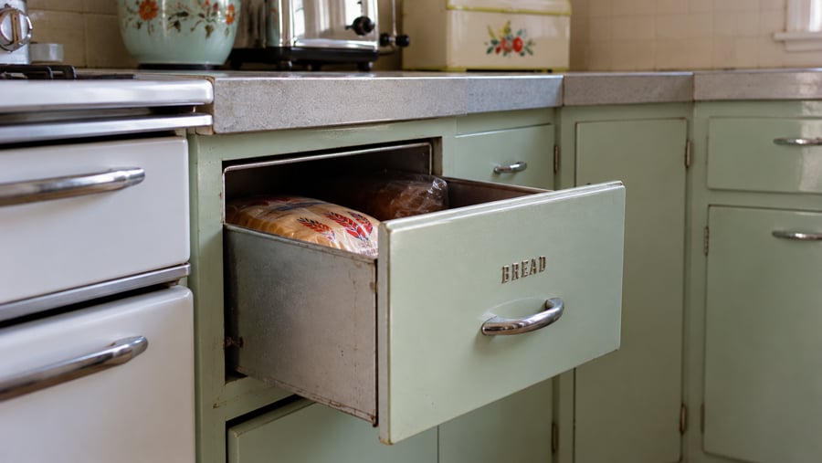 A pale green kitchen drawer labeled “BREAD” pulled open to reveal loaves of bread inside.