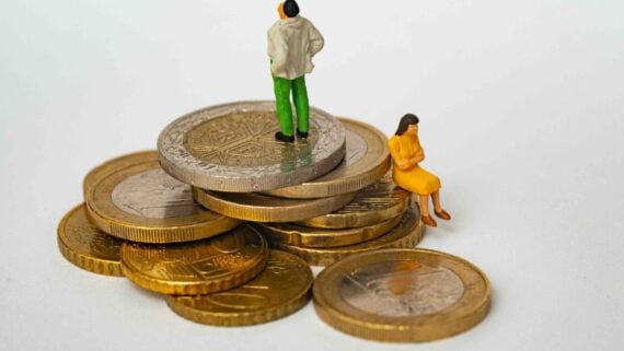 Two miniature figures stand and sit on a small pile of gold-colored coins.