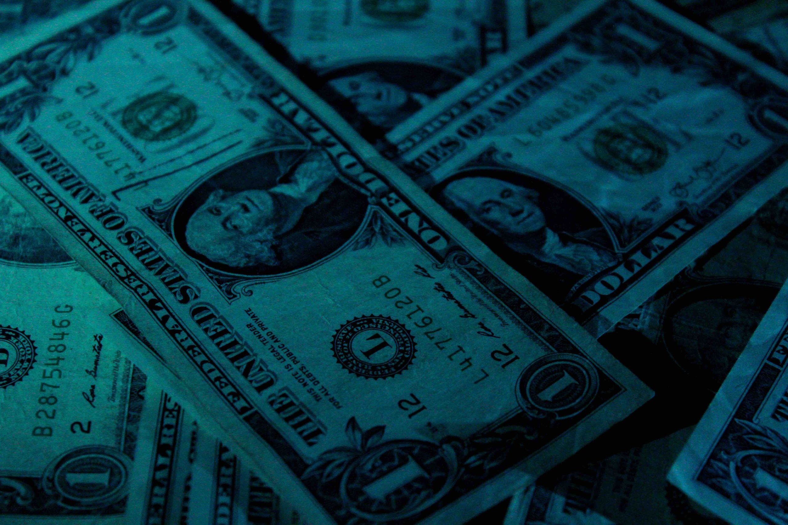 A pile of one-dollar bills illuminated by blue light.